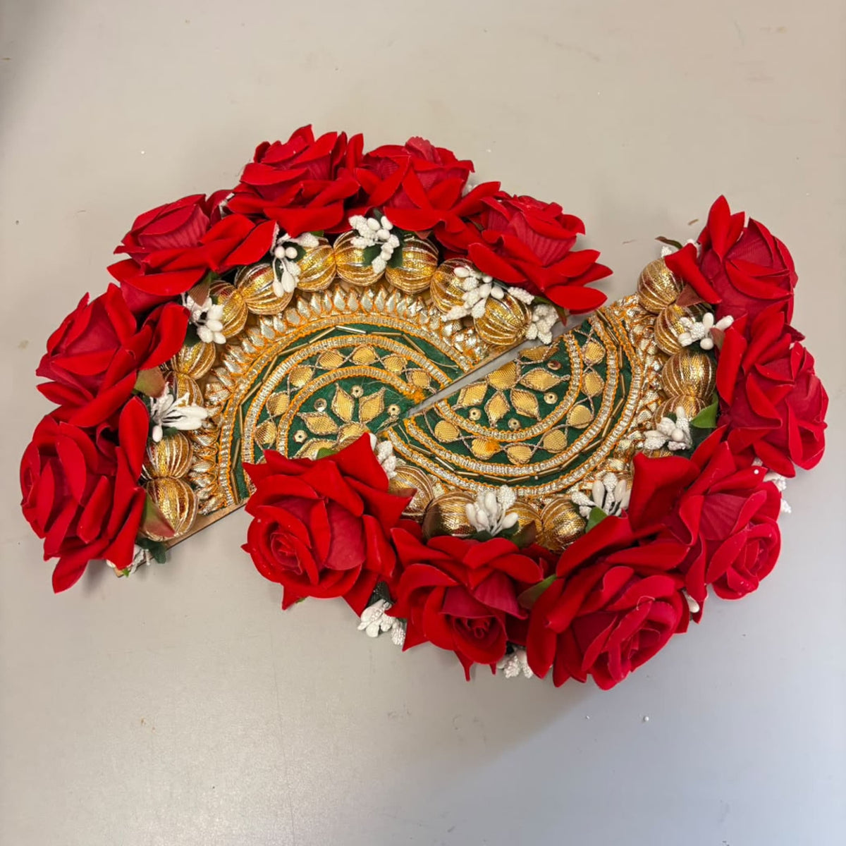 A vibrant red floral decorative rose rangoli centrepiece with gold and green embroidered patterns for Diwali decor