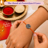 Silver-toned circular floral charm with black scrollwork on bright orange cord designer handmade rakhi for brother and bhabhi