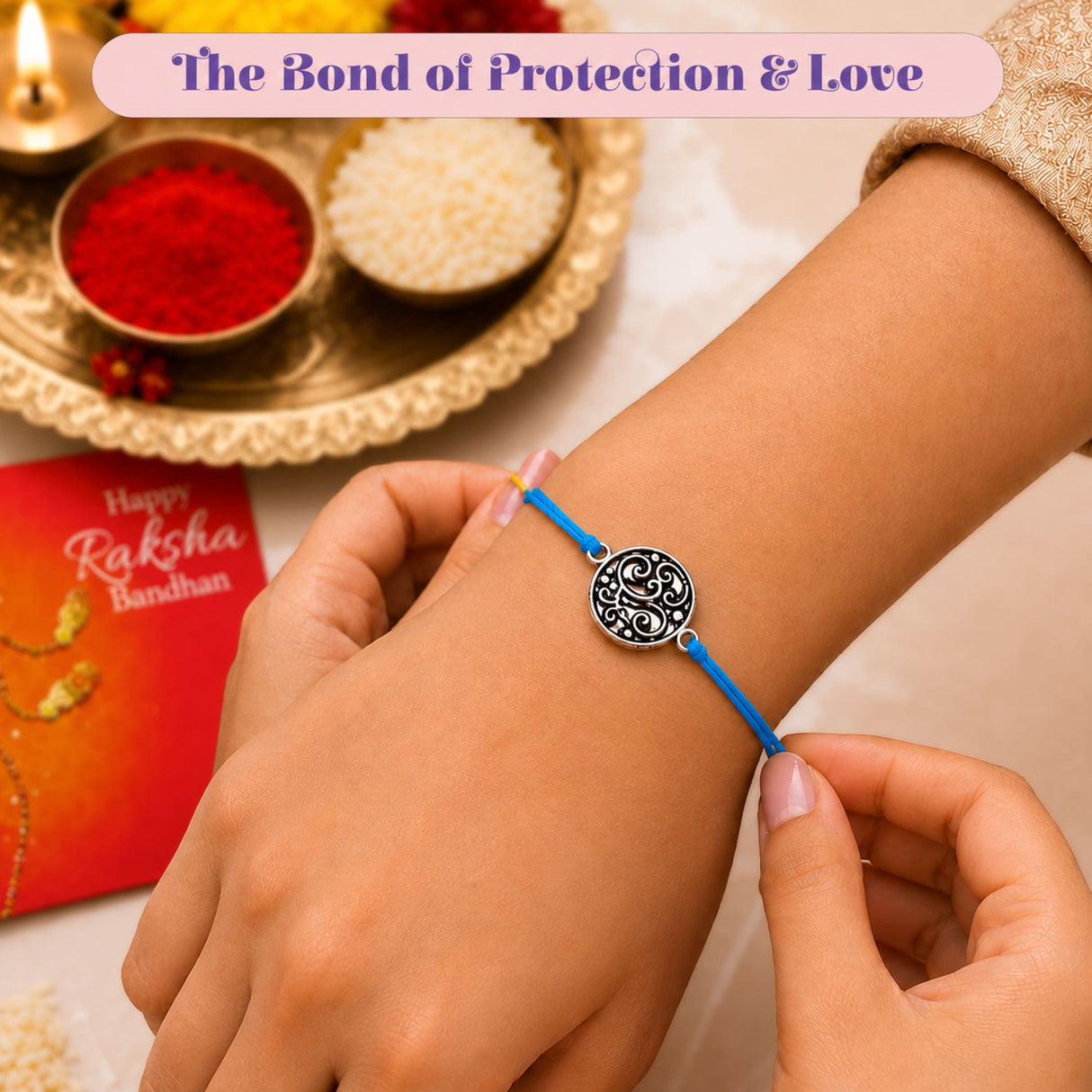A delicate blue cord rakhi bracelet with a circular silver charm featuring intricate black scrollwork design