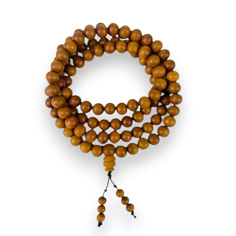 A coiled set of warm amber brown sandalwood mala beads with a polished finish and small tassel for meditation use