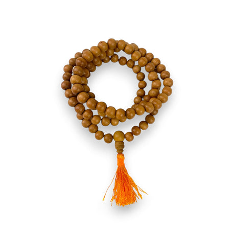 A coiled sandalwood mala with 108 warm brown beads and a vibrant orange tassel used for meditation and prayer