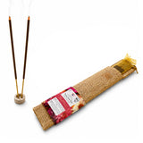 Brown incense sticks with golden tips in wooden holder beside burlap packaging with floral design for spiritual pooja use