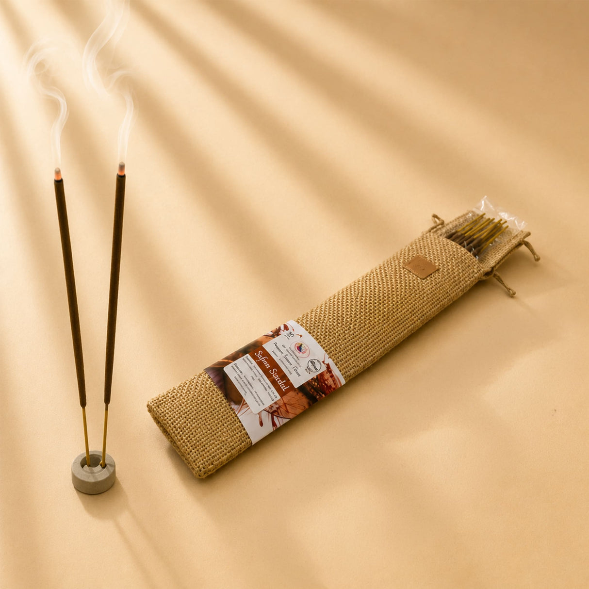 Two slender dark brown premium scented incense sticks with golden tips in a gray ceramic holder for pooja use
