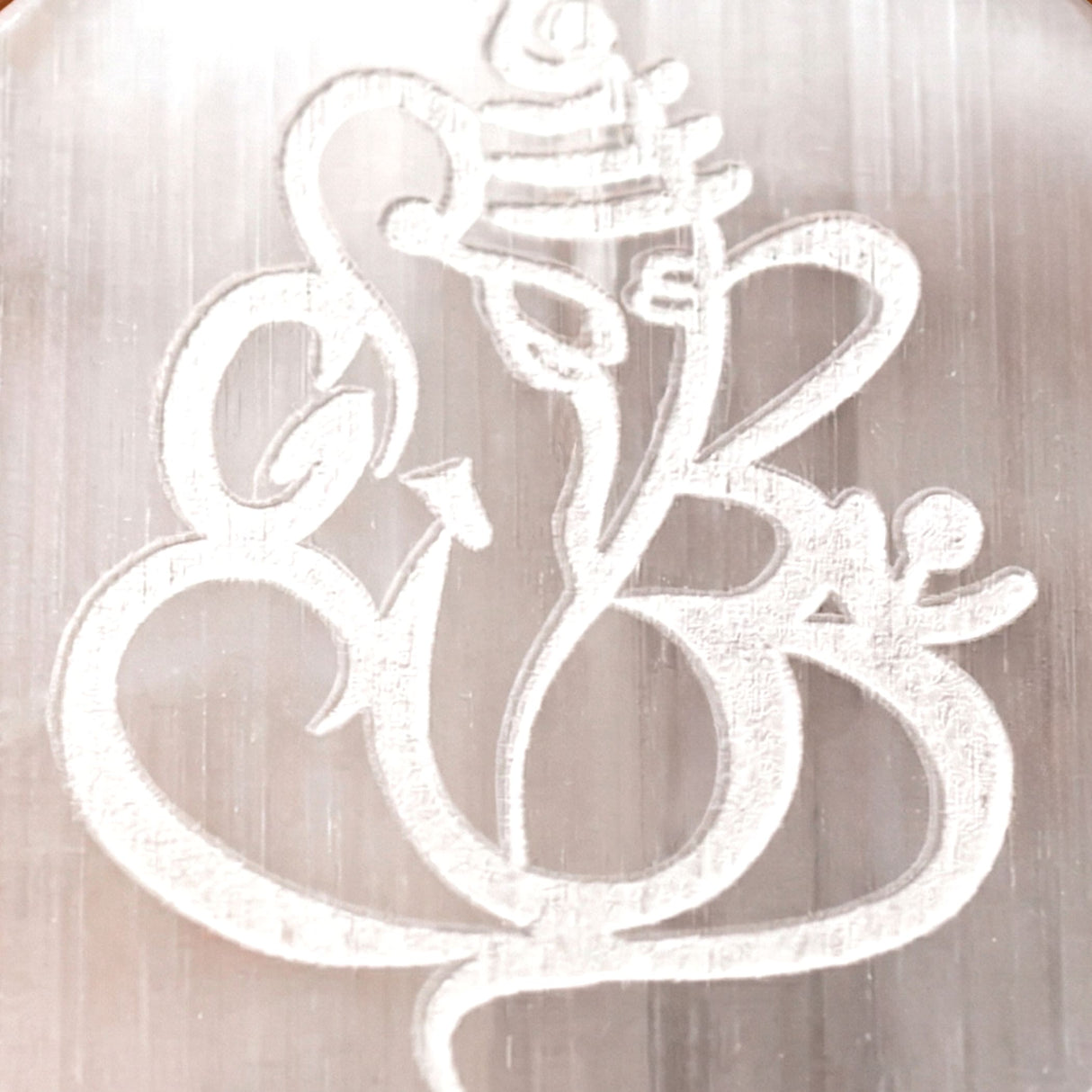 Silver metallic engraved ganesha charm with intricate detailing on a polished selenite charging plate for crystals