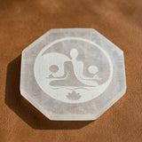A translucent frosted selenite charging plate octagonal with etched meditating figures lotus flower design for healing stones