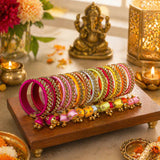 A vibrant collection of silk thread bangles in magenta yellow and pink with gold-tone kundan embellishments and latkan charms