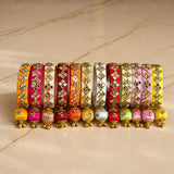 A vibrant array of silk thread bangles in orange pink red and yellow with gold-tone kundan embellishments and latkan tassels