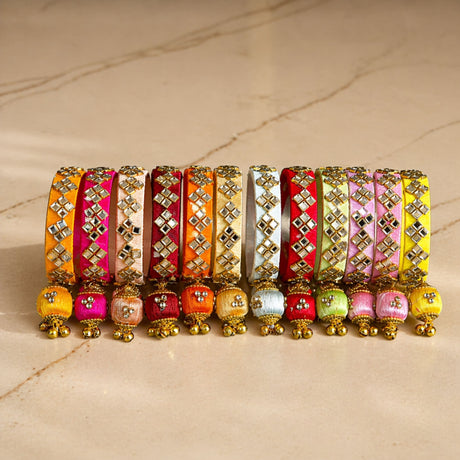 A vibrant array of silk thread bangles in orange pink red and yellow with gold-tone kundan embellishments and latkan tassels
