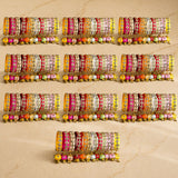 A set of vibrant silk thread bangles in pink orange yellow and white with kundan embellishments and colorful latkan beads