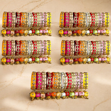 A collection of vibrant silk thread bangles in pink yellow orange and red with gold kundan embellishments and jingle bells