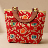 Red silk handbag with intricate gold and teal floral embroidery and wooden handles for traditional Indian festivals