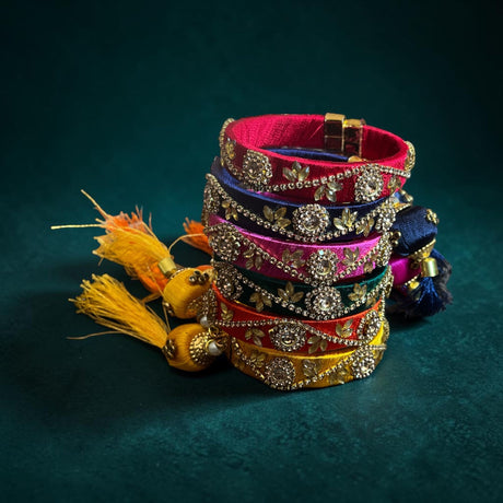 A stack of vibrant silk thread bangles in pink purple red and gold with kundan-style work and silver floral designs