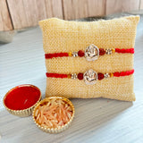 Designer silver tone ganesha rakhi set featuring two red and silver bracelets displayed on a beige jute pillow