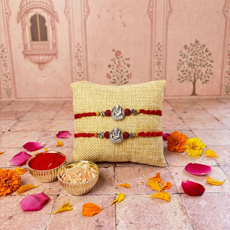 Two red thread rakhi bracelets with silver ganesha charms and beads on a beige cushion designer silver tone set for brother