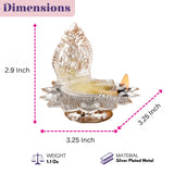 Silver-plated metal lakshmi diya with intricate floral and deity carvings featuring a flame in the oil-filled basin for puja