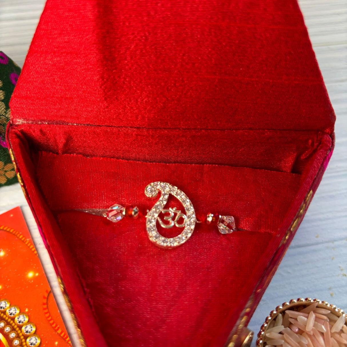 A sparkling silver om rakhi with clear crystals in a red velvet box for raksha bandhan protection and good luck