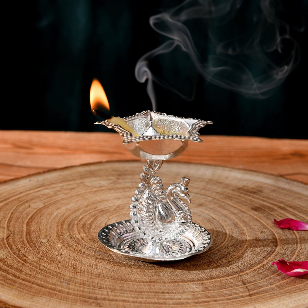 Silver plated peacock diya oil lamp with intricate engravings and lit flame emitting smoke for home pooja mandir