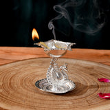 Silver plated peacock diya oil lamp with intricate engravings and lit flame emitting smoke for home pooja mandir