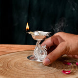 Silver plated peacock diya oil lamp with intricate design and lit wick for home pooja mandir and Diwali decor