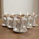 Silver plated peacock diya oil lamp with intricate engravings and lit candles for home pooja mandir and diwali decor