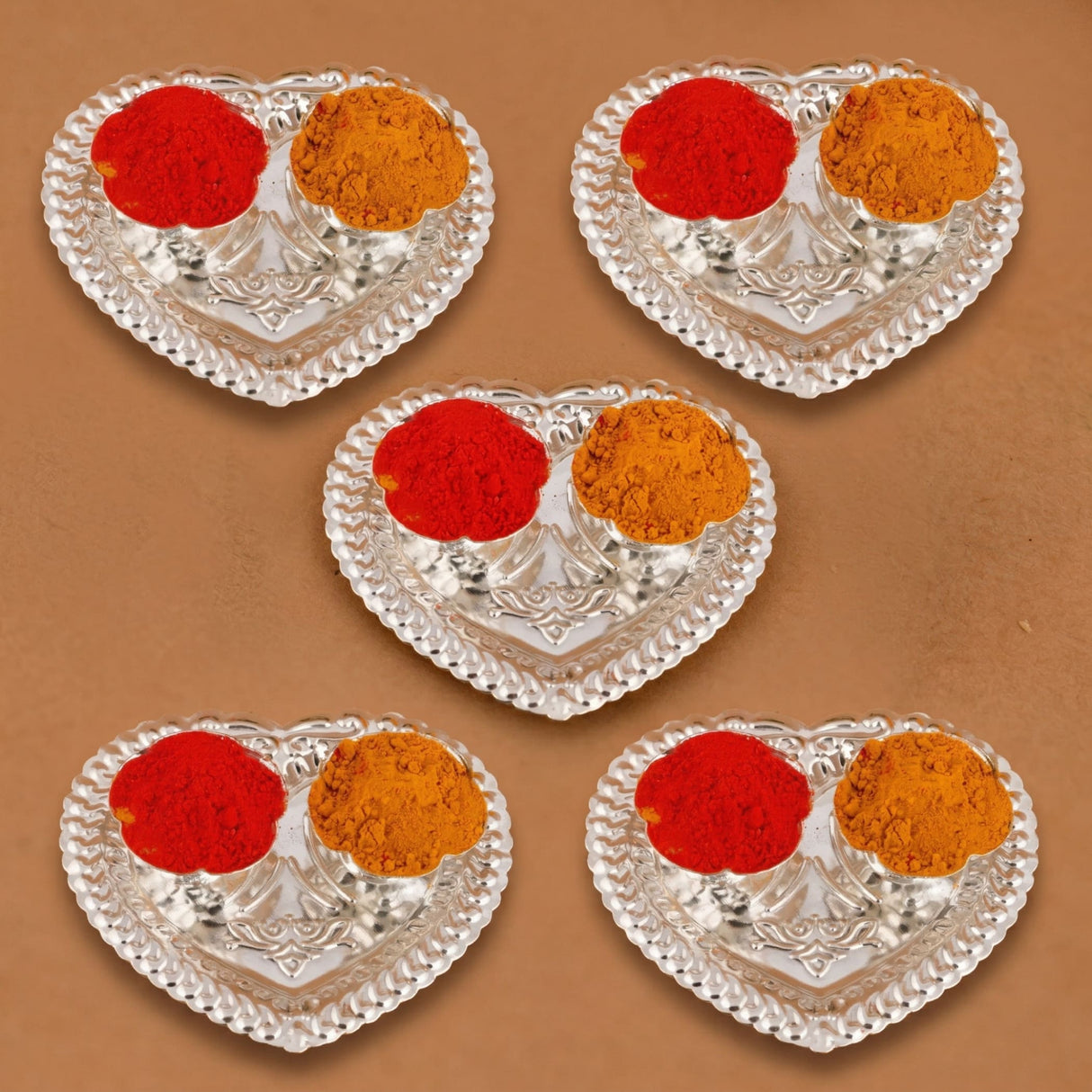 Silver plated heart-shaped haldi kumkum holder with intricate embossed patterns holding red and orange powder for puja decor