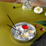 Silver plated metallic pooja thali tray with three compartments holding red powder rice grains and a lit decorative diya