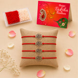 Four red cord rose charm rakhi bracelets with silver metal roses displayed on a burlap pillow for raksha bandhan