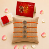 Four orange cord rakhi bracelets with silver rose-shaped charms on burlap pillow for brother and bhabhi gift