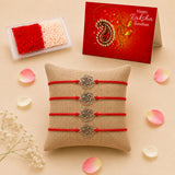 Four red cord rakhi bracelets with silver rose-shaped metal charms arranged on a burlap pillow for brother and bhabhi