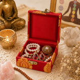 Small handmade red velvet jewelry box with gold paisley trim and brass clasps holding pearl bracelets and red earrings