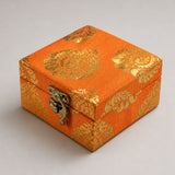 Small handmade jewelry box with orange brocade fabric, gold floral pattern, and silver clasp for indian wedding favors