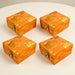 Four vibrant orange fabric boxes with intricate gold gota patti brocade floral patterns and metallic clasps for gifts