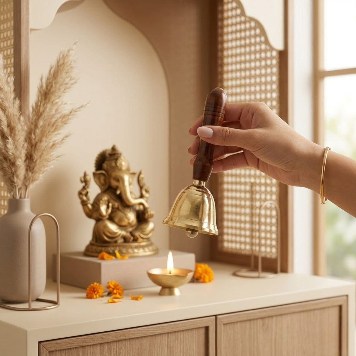 A hand holds a polished solid brass bell with a dark wooden handle used for prayer school weddings and pooja rituals