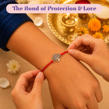 A silver tree of life charm on a vibrant red cord rakhi bracelet being gently adjusted on an arm for raksha bandhan