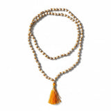 A delicate white and gold beaded tulsi holy basil japa mala necklace with a vibrant orange tassel for meditation and yoga