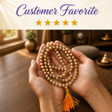 A delicate beige and orange tulsi holy basil japa mala necklace with matching tassel held in cupped hands for meditation