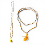 A long 5 mm tulsi mala beads necklace with alternating white and gold beads and a vibrant yellow tassel for meditation