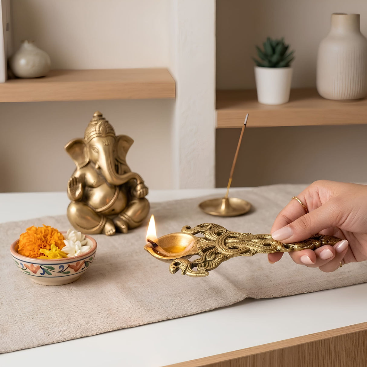 Golden ornate brass pooja aarti spoon with intricate filigree twin peacock design and lit flame for diya and hawan use