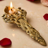Golden brass pooja aarti spoon diya with intricate peacock and floral engravings holding a lit candle for hawan rituals