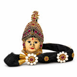 Golden ornate vara lakshmi goddess face headpiece with red clear gemstones white floral embellishments and black tassel for temple pooja