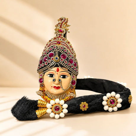 Vara lakshmi goddess face set with decorative black headpiece featuring gold accents red gemstones and pearl flowers for pooja
