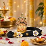 Golden and red jeweled Vara Lakshmi goddess face with intricate headpiece and black fabric with white floral embellishments