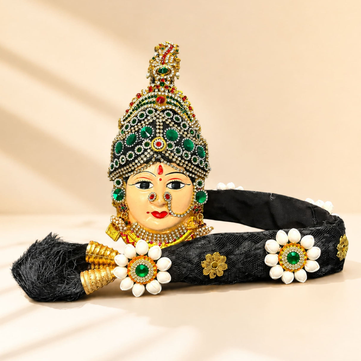 An ornate black Vara Lakshmi goddess face headpiece with jeweled accents and floral embellishments for Navaratri pooja
