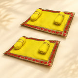 Bright yellow velvet pooja aasan mats with embroidered red and gold borders and matching cylindrical cushions for laddu gopal
