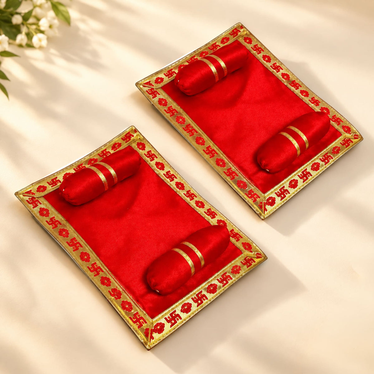Pack of 2 red velvet pooja aasan trays with gold trim and embroidered swastika holding red cylindrical objects for laddu gopal