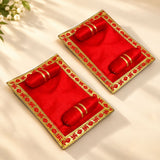 Pack of 2 red velvet pooja aasan trays with gold trim and embroidered swastika holding red cylindrical objects for laddu gopal