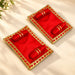 Pack of 2 red velvet pooja aasan trays with gold trim and embroidered swastika holding red cylindrical objects for laddu gopal