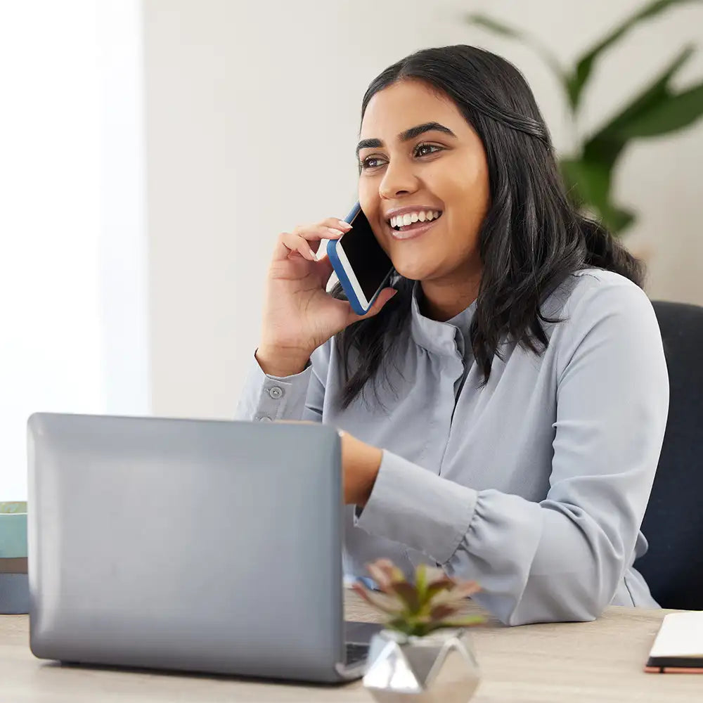 Smiling woman on a phone call while working on a laptop.