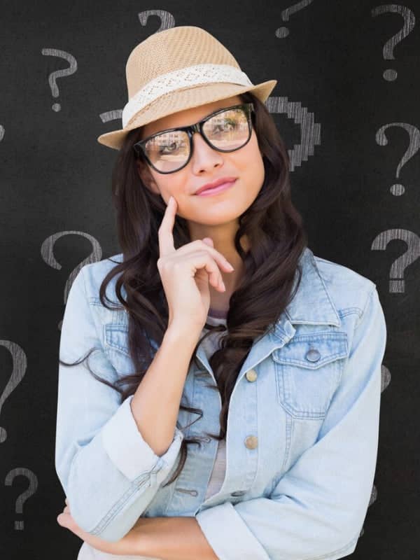 Woman wearing a straw hat, glasses, and denim jacket with a thoughtful expression.