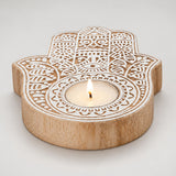 A light wood hamsa hand-shaped tea light candle holder with intricate white carvings for Diwali decoration